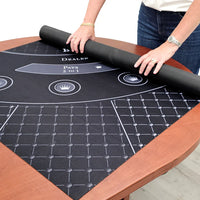 Person rolling out a black neoprene blackjack table cover on a wooden table.