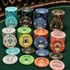 A collection of stacked Gatsby Room casino ceramic poker chips in multiple colors and denominations arranged on a green felt table with a brown leather chair visible in the background.